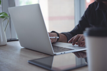 Close up of business man using, typing on laptop computer keyboard, online working from home office with digital tablet on wooden table
