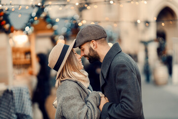 Christmas couple having romantic moments outdoors on Christmas. A young couple is standing on the street, holding hands and giving Eskimo kisses on New Year's Day. - obrazy, fototapety, plakaty