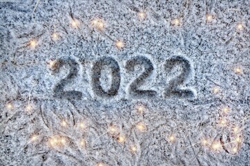 Inscription 2022 on a snow-covered surface with christmas lights. Happy new year 2022 concept.