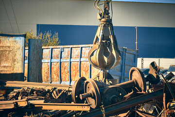 Magnet crane unloads scrap metal from truck. Hand of grabber excavator unloading recycle metal waste from truck. Clamshell at scrap metal yard
