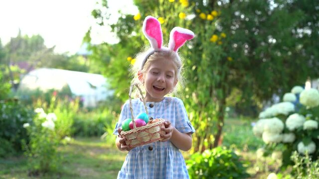 a little blonde girl with bunny ears holding a basket of painted Easter eggs in her hands and laughing, the concept of a religious holiday