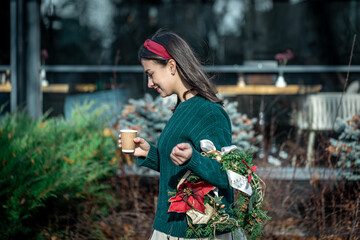 Young woman with a Christmas wreath and a cup of coffee on a city walk.