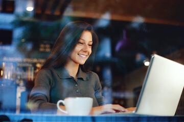 Adorable young cute woman and using laptop at coffee shop. Cheerful businesswoman working at a cafe