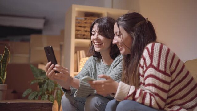 A female couple makes a video call to their new home during the move. Happy friends sharing their joy with family making a call with a smartphone.