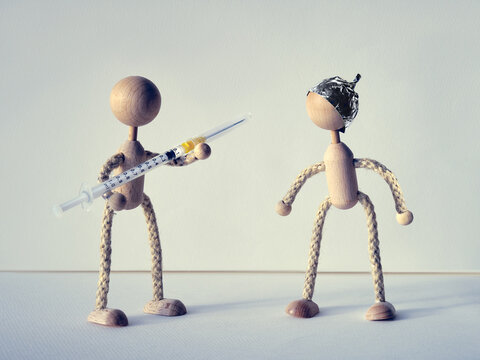 Vaccination discord in society, creative concept. Wooden toy figurines of medic with syringe and corona septic, anti vax activist in tin foil hat.