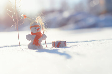 Christmas toy snowman with gifts standing on winter snowy landscape shining in the sun. Merry christmas and happy new year greeting card