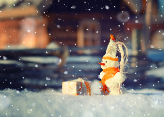 Christmas cute snowman standing near miniature toy house on winter Christmas street landscape. A toy scene like from a hand-drawn cartoon. 