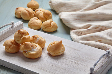 Appetizing profiteroles with whipped cream on a white wooden tray