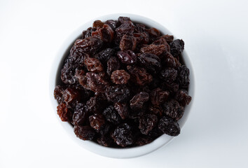 Top view of portion of dried dark raisins in white ceramic pot, on white background