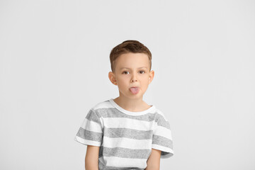 Portrait of cute little boy showing tongue on light background