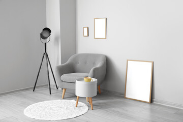 Blank frames, grey armchair with table and lamp near light wall