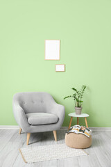 Grey armchair, pouf, table and blank frames hanging on green wall