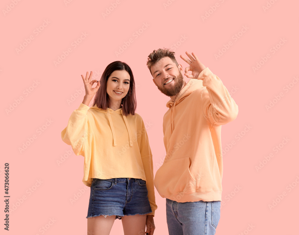 Wall mural Cool young couple in hoodies showing OK on color background - Wall murals