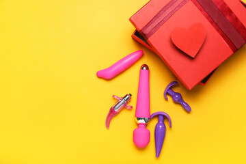 Box and toys from sex shop on color background