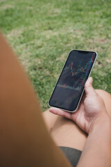 Girl holding a smartphone with financial stock market graph on the screen in the park. Stock Exchange