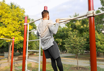 Fototapeta premium Young man doing chin-up on sport ground