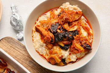 Bowl with delicious oatmeal, gravy, beef stew and prunes on light table