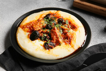 Plate with delicious mashed potatoes, gravy and beef stew with prunes on grey table