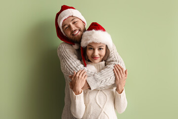 Happy young couple in stylish winter clothes and Santa Claus hats on color background