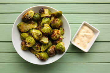 Bowl with tasty roasted Brussels cabbage and sauce on color wooden background