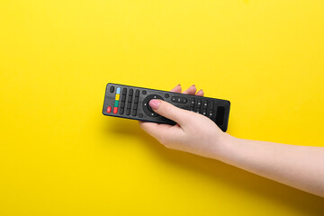 Woman pressing button on TV remote controller on yellow background