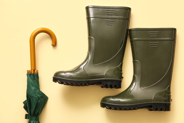 Pair of rubber boots and umbrella on color background, closeup