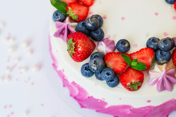 Delicate cake garnished with fresh strawberries blueberries on a pink plain background. Festive dessert with berries