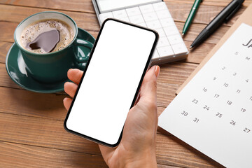Female hand with mobile phone, paper calendar and cup of coffee on wooden background