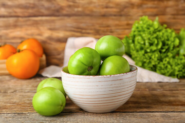 Bowl of fresh green tomatoes on wooden background