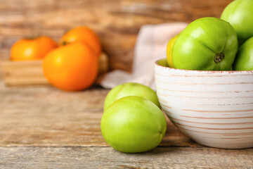 Bowl of fresh green tomatoes on wooden background, closeup