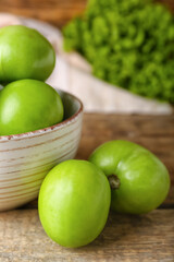 Bowl of fresh green tomatoes on wooden background, closeup
