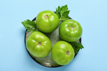Plate with green tomatoes and parsley on blue background