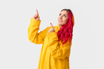 Beautiful woman in raincoat pointing at something on light background