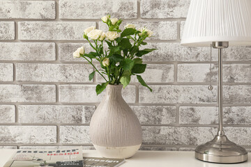 Vase with bouquet of roses on table near brick wall