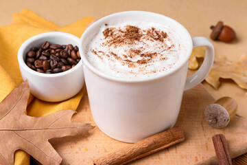 Cup of tasty coffee with cinnamon and beans on beige background