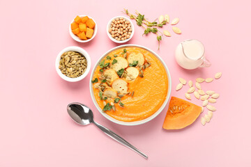 Composition with delicious pumpkin cream soup in bowl and seeds on pink background