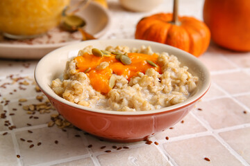 Bowl of tasty oatmeal with pumpkin on tile background