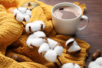 Branch of cotton flowers, cup of coffee and knitted sweater on wooden table, closeup
