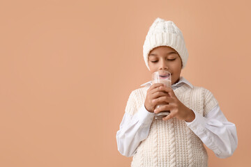 African-American boy in winter clothes drinking tasty hot chocolate on color background