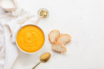 Bowl of tasty pumpkin cream soup and bread on white background