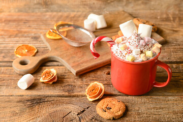 Cup of tasty cacao with marshmallows and candy cane on wooden background