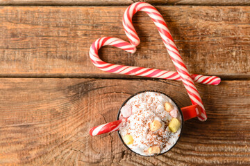 Cup of tasty cacao with marshmallows and candy canes on wooden background