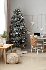 Interior of room with modern workplace and Christmas tree near grey wall
