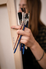 One young caucasian woman female artist professional or amateur painter student painting at home holding paintbrushes in hand posing with copy space close up focus on hand with brushes