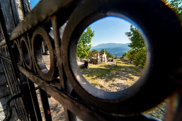 Fototapeta premium Mountainside Cemetary seen through the hole of an iron fence,central Montenegro,Eastern Europe.
