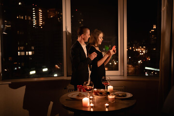 Couple in love celebrating valentine's day dinner with candles, anniversary or date at night in a restaurant, dark windows background, passionate man hugging woman