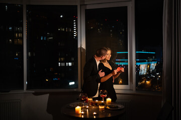 Fototapeta na wymiar Romantic date at night on valentine's day, dinner for two with candles, couple standing by panoramic windows, adult young silhouettes by the window