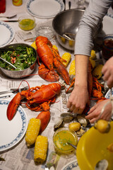 Hands Reaching for Clam and Lobster Bake on Table Covered in Newspaper