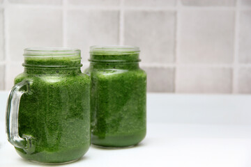 Green juice made from vegetables such as cucumber, lemon, spinach, chard, celery served in a glass mason jar for a healthy, vegan and nutritious breakfast
