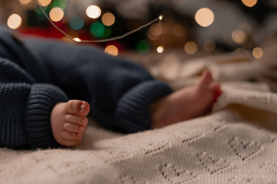 bare feet of a baby in a blue knitted jumpsuit lying on a light blanket on the floor under the Christmas tree closeup. winter holiday, funny moments, child christmas. High quality photo